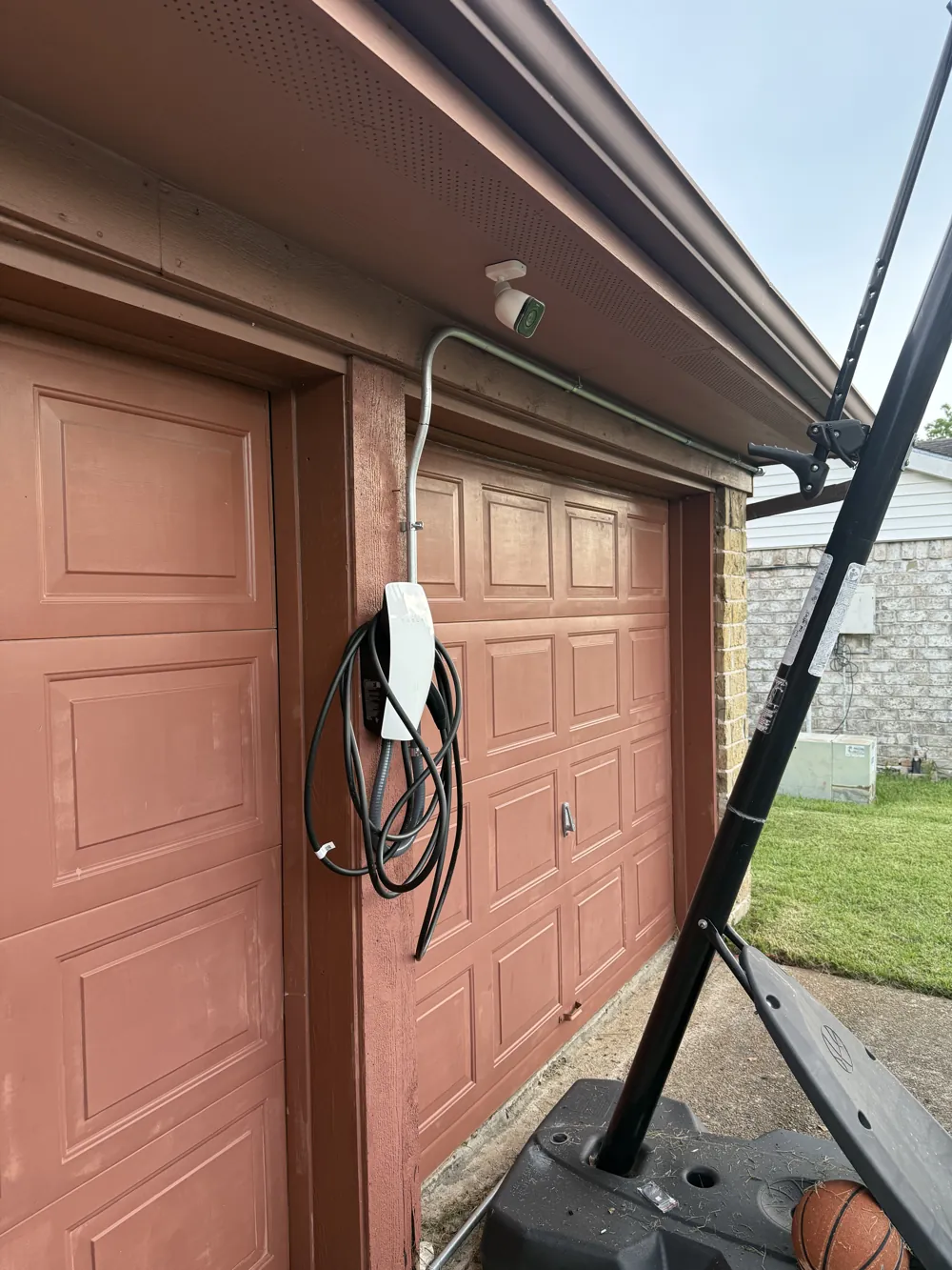 Wall-mounted home EV charger beside a garage door with exterior conduit